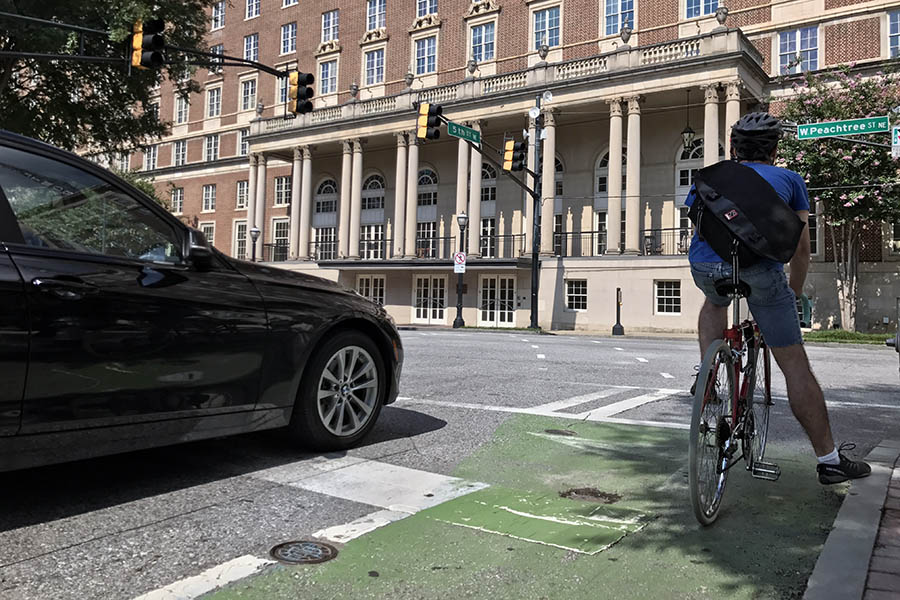 A bicyclist waits at a stop light in a green-painted bike lane in Midtown Atlanta. These kinds of lanes are designed to draw attention to bicyclists and identify potential points of conflict between bikes and vehicles. A just-published study from Georgia Tech transportation engineering researchers has found that engineers and planners lack the data they need to truly understand whether these kinds of interventions make cyclists safer. (Photo: Jess Hunt-Ralston)