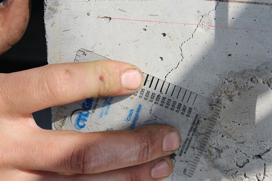 A researcher measures the width of a crack in a reinforced concrete column after testing the strength of the column. A new project funded by the U.S. Department of Energy Advanced Research Projects Agency will develop a field-deployable tool to detect cracks far smaller than this — and inside rather than outside — thick reinforced concrete structures. Finding these microcracks before they become larger cracks will allow for preemptive repairs that vastly improve the concrete's durability and save millions of dollars for owners of power plants, bridges, dams and other larger concrete structures. (Photo: Chris Kiser)