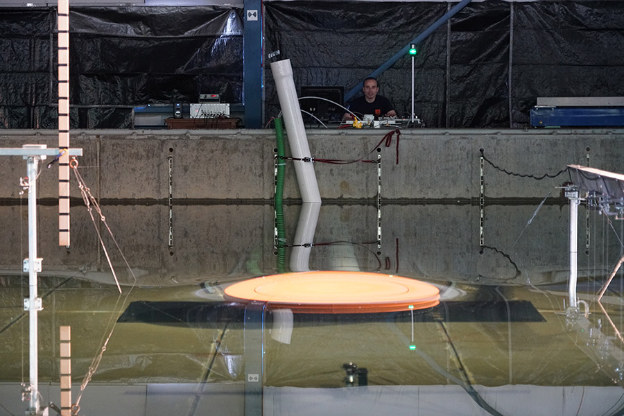 The water surface bows upward as Professor Hermann Fritz, background, launches the volcanic tsunami generator from the control stand in the Hinsdale wave basin at Oregon State University. Fritz and collaborators at the University of Oregon and Texas A&M University at Galveston are using the data from these experiments to understand how underwater volcanoes generate tsunami waves and improve predictive models. (Photo: Angela Del Rosario)