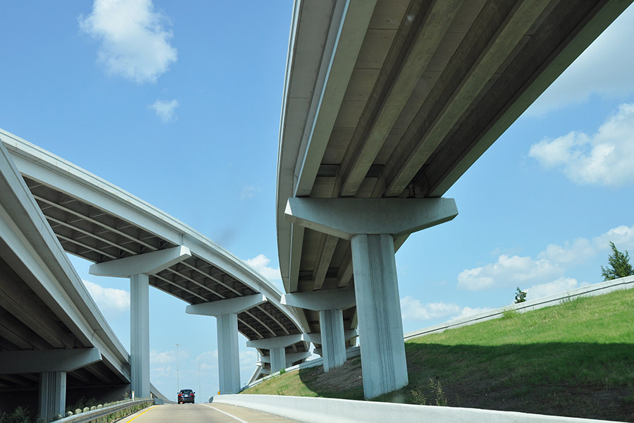 Looking up at several levels of highway bridges and overpasses stretching across roads with blue sky above. (Photo Courtesy: Drriss & Marrionn via Flickr)