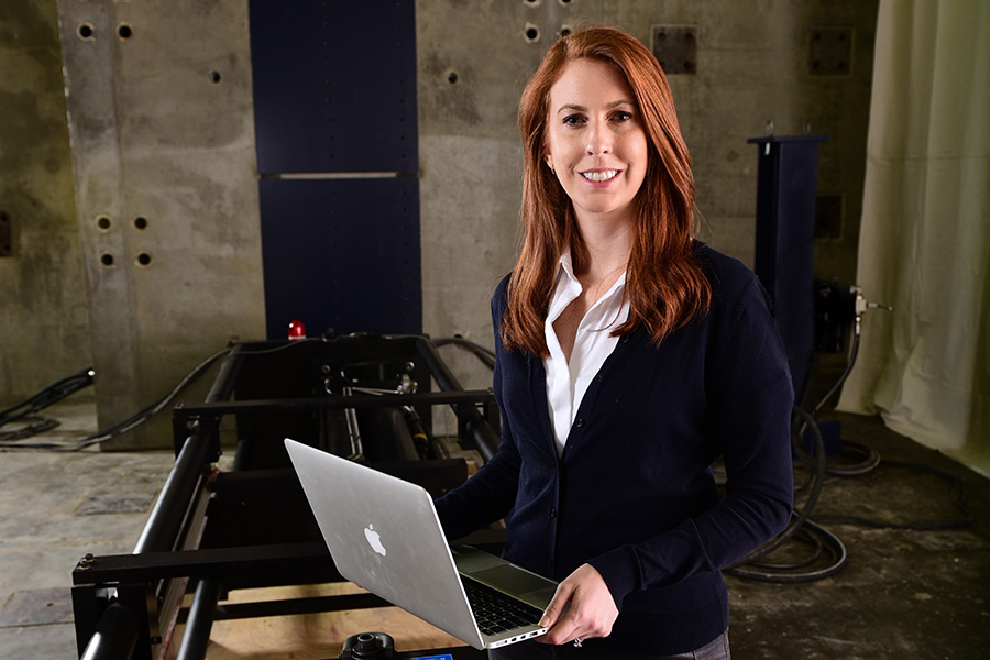 Lauren Stewart stands with a laptop in the Structural Engineering and Materials Lab. (Photo: Gary Meek)