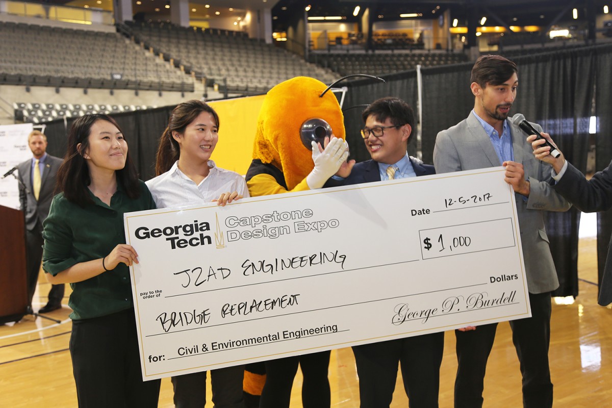 Team J2AD Engineering won the civil and environmental engineering award at the fall 2017 Capstone Design Expo. From left, Jessie Lei, Jiyoon Oh, Austin Foo and Donald Smith accept their winnings from Buzz (yellow jacket, center). (Photo: Jess Hunt-Ralston)