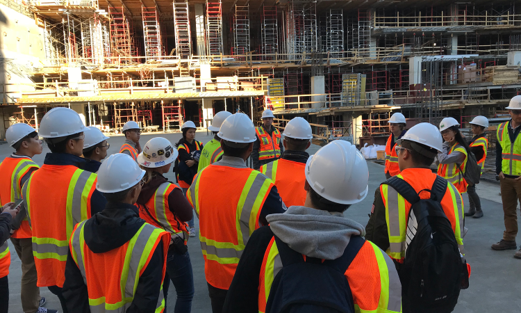 A group of people wearing hard hats and reflective vests stand in front of a construction site