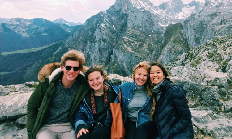 Four people pose for a photo in front snow-capped mountains