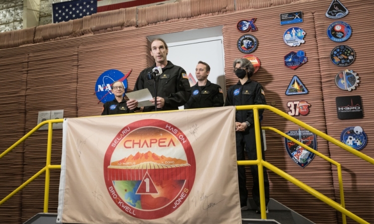 A man speaks at a microphone as part of a NASA crew 