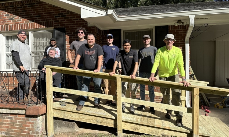 Crew of CEE faculty, staff and students pose on newly constructed wheelchair ramp in front of house.