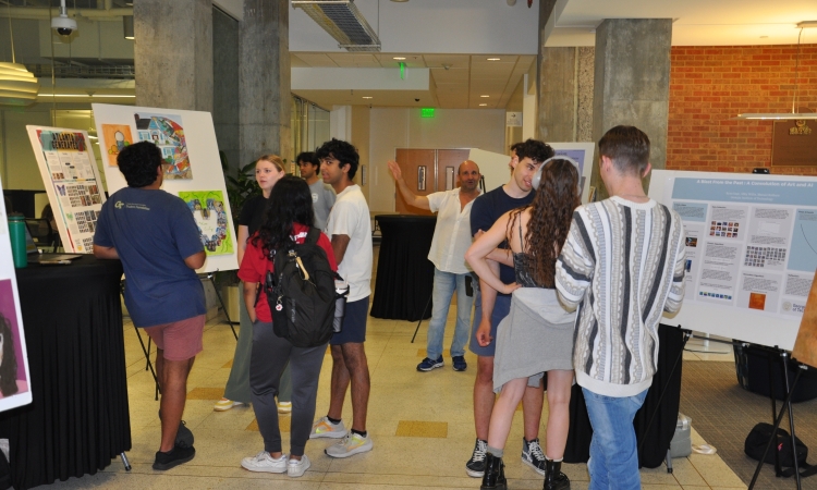Students mingling in the Mason lobby looking at artwork and project displays on easels. Professor Francesco Fedele is standing in the rear.