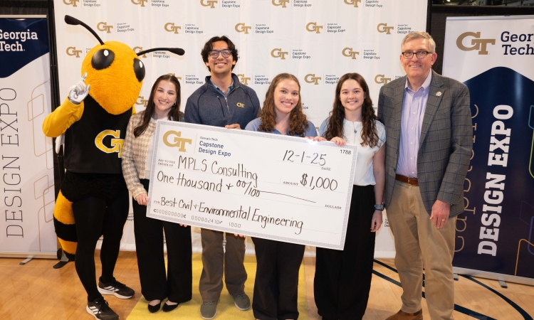 Buzz, the yellow jacket mascot, poses with four students holding an oversized prize check and a Professor