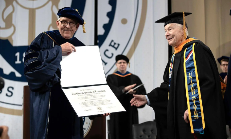 An elderly man in cap and gown receives a diploma from another man in cap and gown