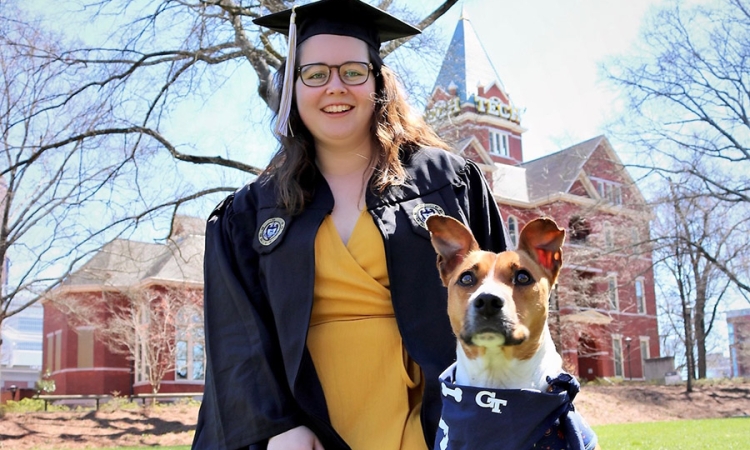 A woman wearing a cap and gown poses with her dog 