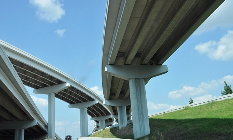 Looking up at several levels of highway bridges and overpasses stretching across roads with blue sky above. (Photo Courtesy: Drriss & Marrionn via Flickr)