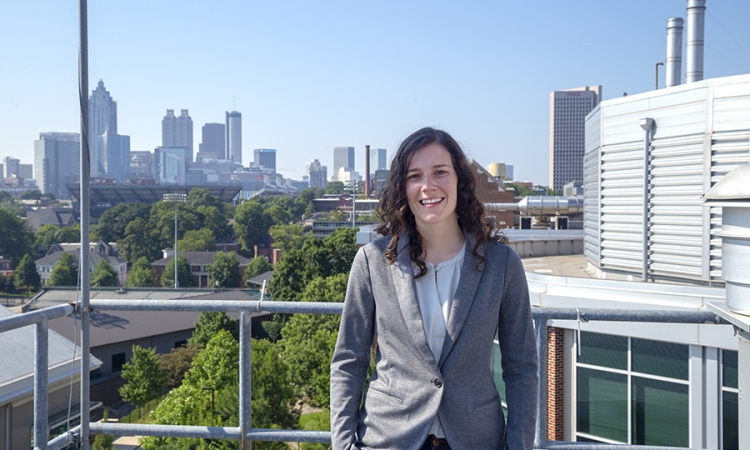 Assistant Professor Jennifer Kaiser, wearing a gray blazer, poses on campus with the Atlanta skyline in the background.