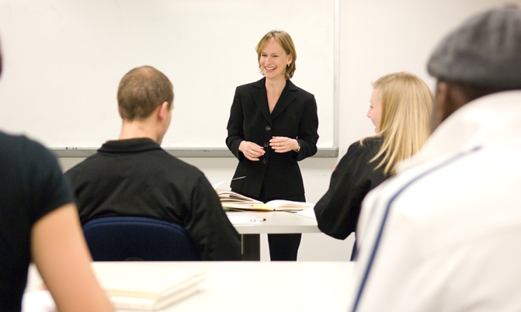 Standing before a white board wearing a black blazer, Lisa Rosenstein leads a class.