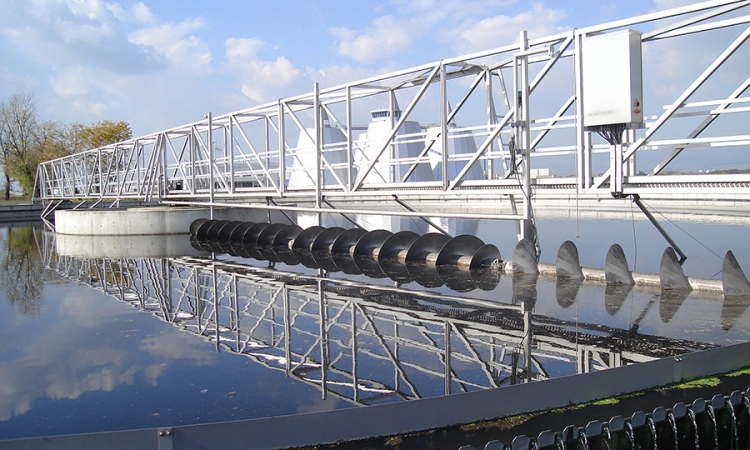 Biological wastewater treatment equipment reflected on smooth water with a blue sky and clouds.