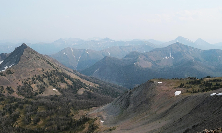 A photo of large mountains with a few trees and small white spots of snow in Yellowstone National Park. 