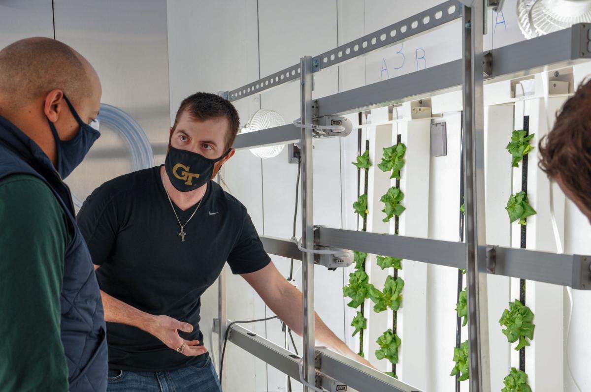 A man wearing a GT face mask shows off hydropaunic lettuce growing in a lab