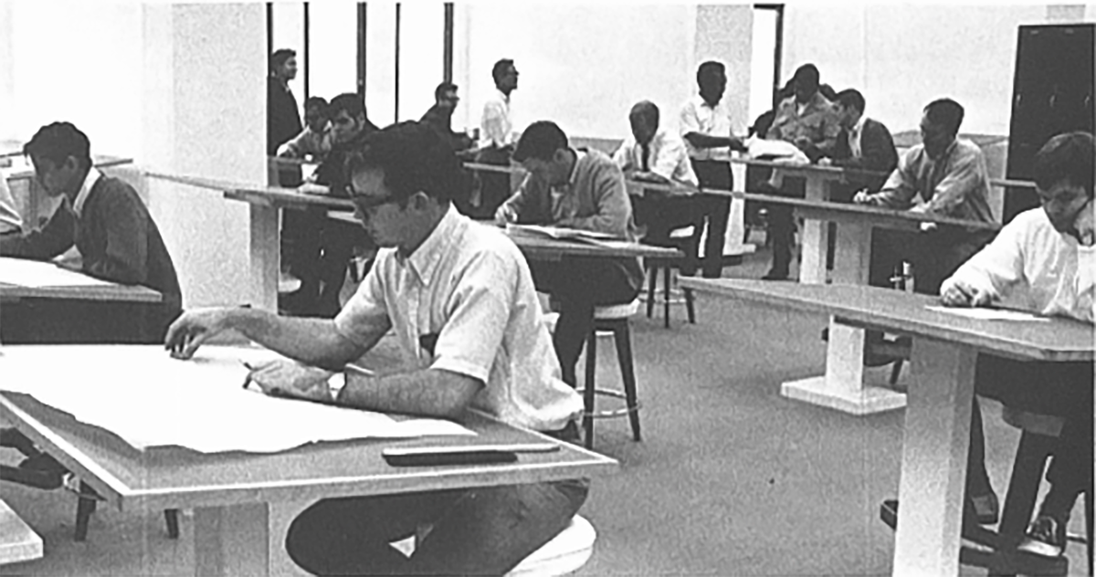 A black and white photo of men working at drafting tables