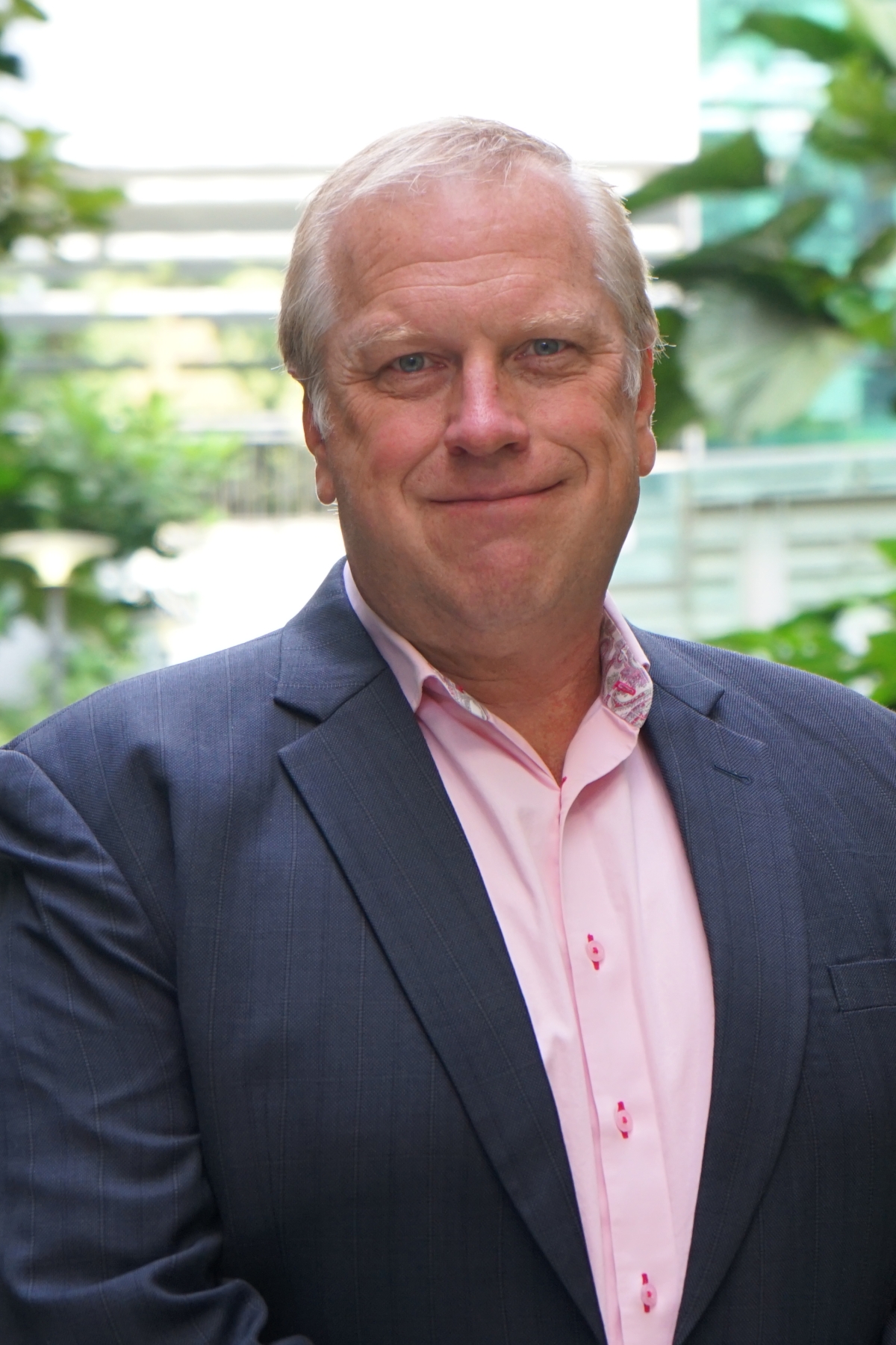 Headshot of a man in a light pink shirt and navy blazer