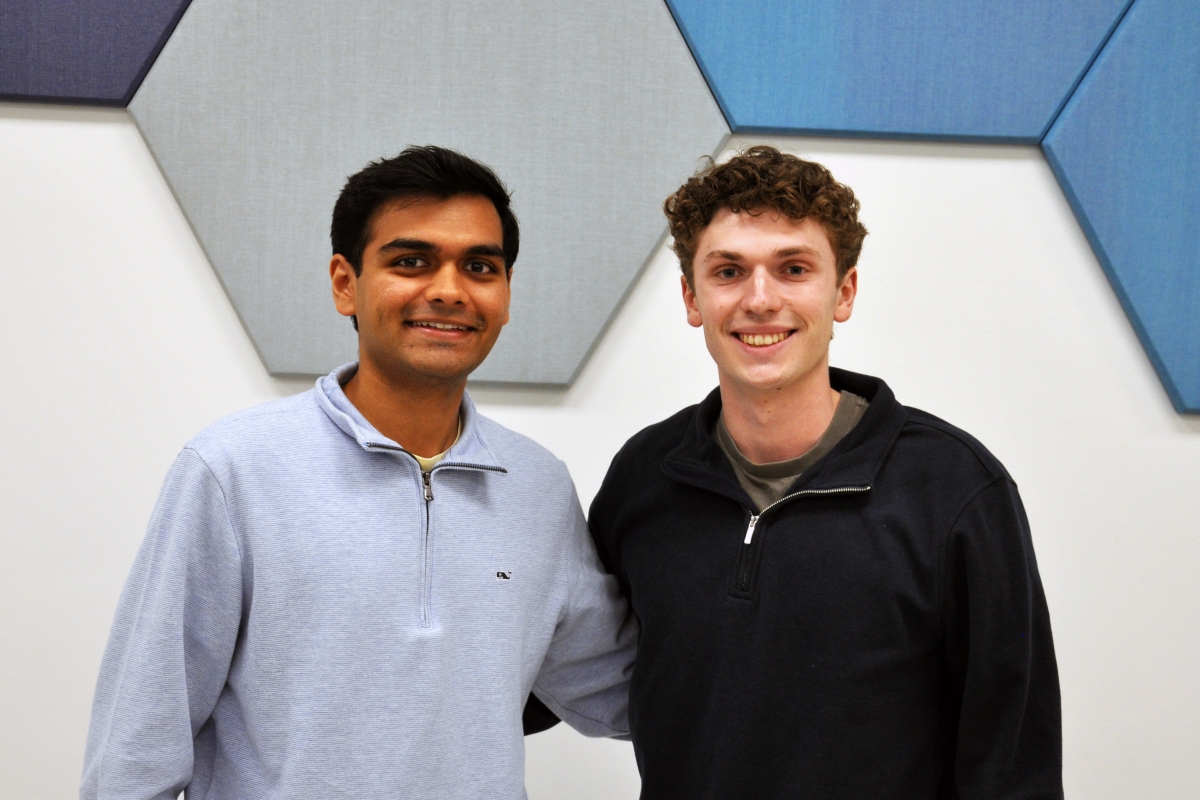 Two people pose in front of blue and gray hexagon tiles 