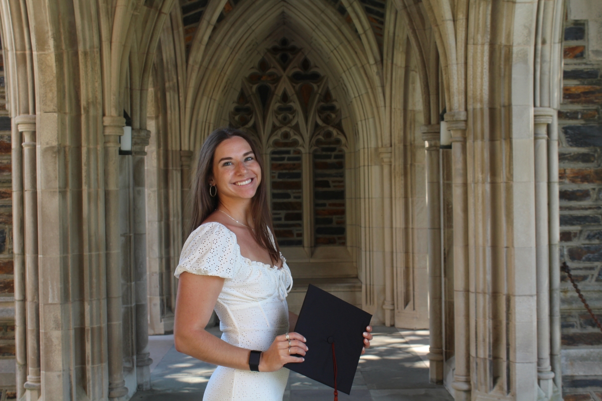Samantha DiLoreto in a white dress holding a mortarboard surrounded by gothic columns from a Georgia Tech building