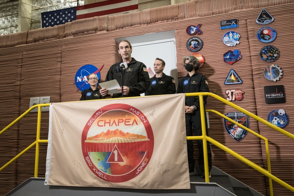 A man speaks at a microphone as part of a NASA crew 