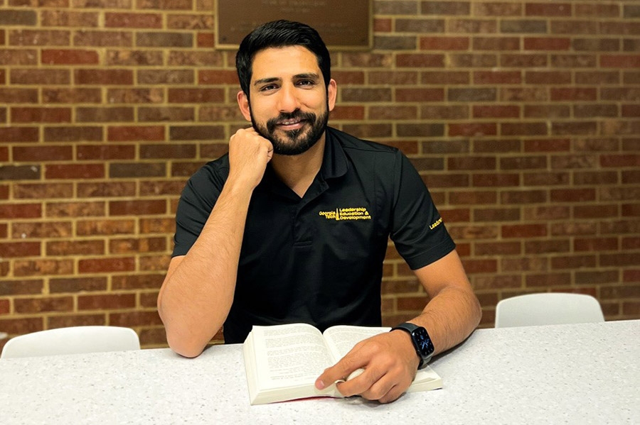 A man sits at a table with a book in front of a brick wall