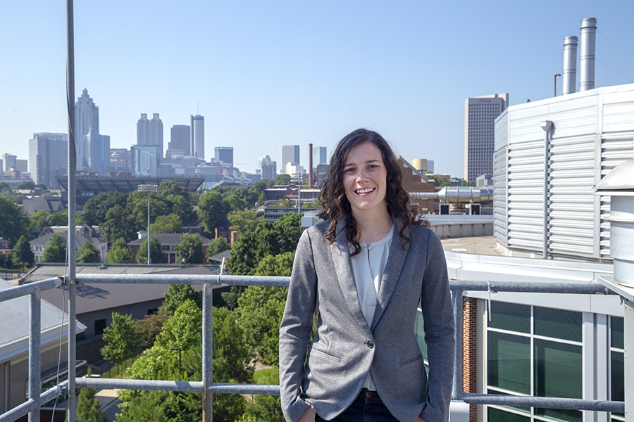 Assistant Professor Jennifer Kaiser, wearing a gray blazer, poses on campus with the Atlanta skyline in the background.