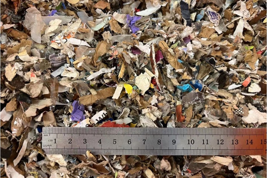 A silver ruler in the lower third of the photograph provides scale for small pieces of municipal solid waste