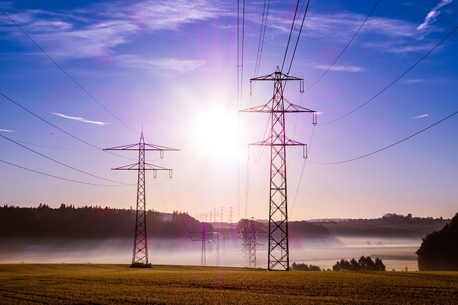 Power poles stretch into a bright sun with mist hovering just above the ground.