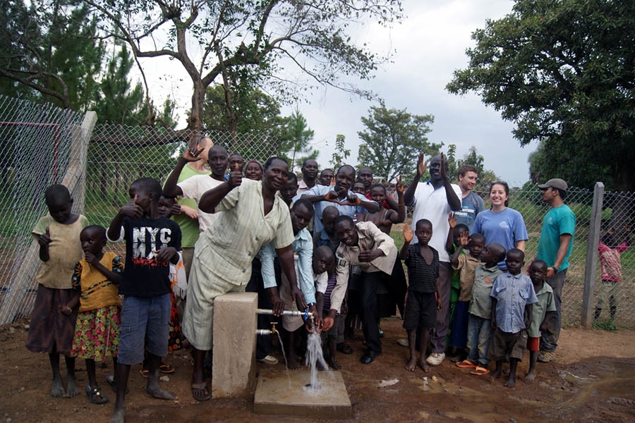 Oloo, Uganda, community members stand with the water pump that Engineers Without Borders has helped them construct.