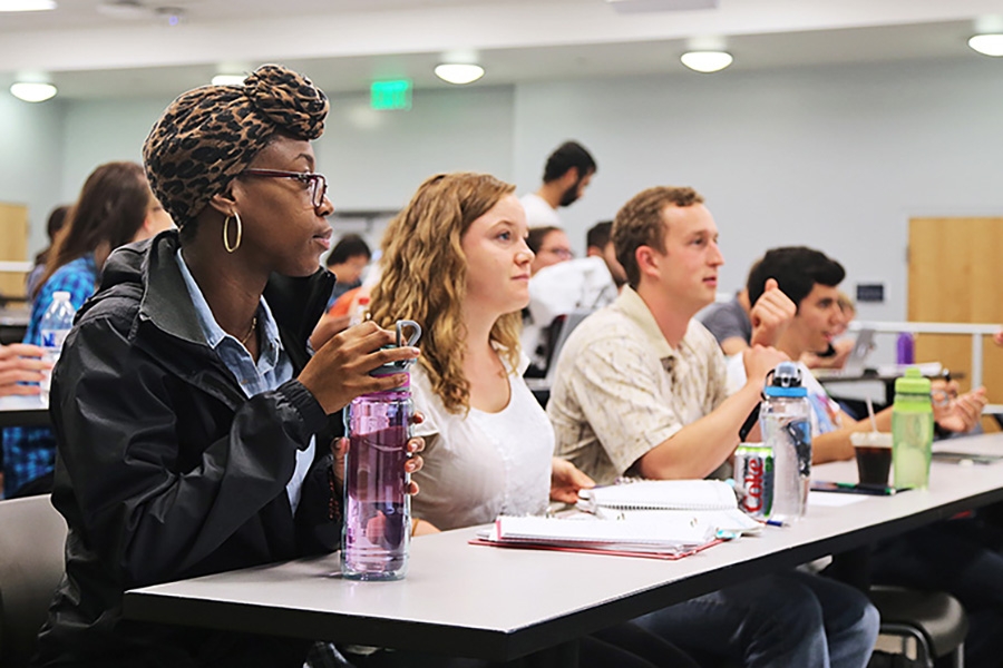 Four students sit attentitively at a long table in a lecture hall