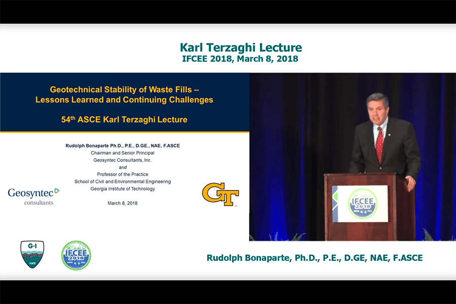 Video screenshot of Rudy Bonaparte delivering the Karl Terzaghi Lecture on March 8, 2018. Split screen shows Bonaparte at a podium on the right and his title slide on the left, "Geotechnical Stability of Waste Fills – Lessons Learned and Continuing Challenges."