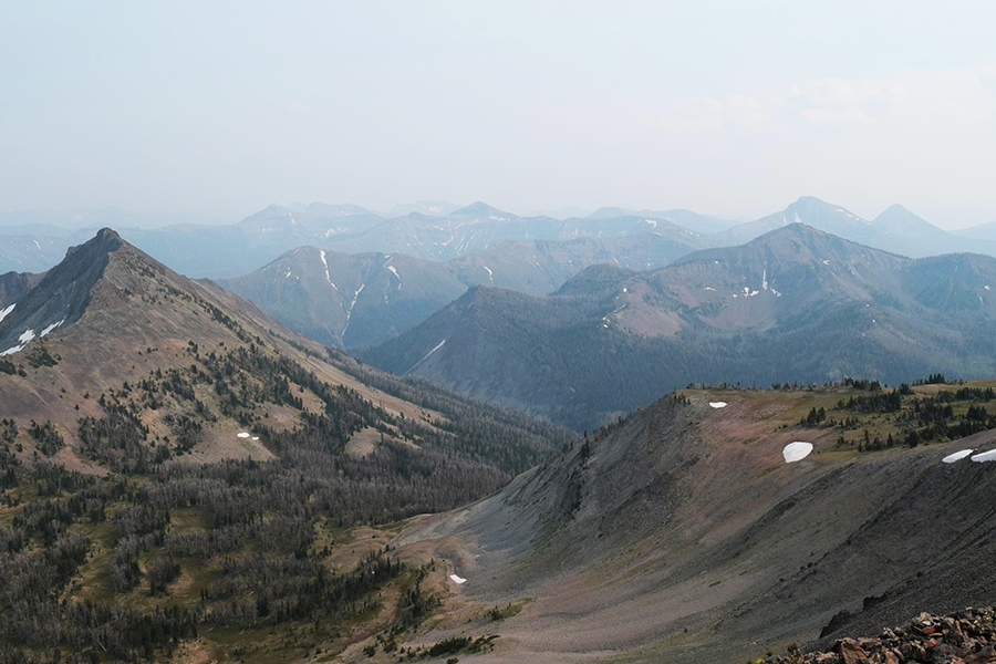 A photo of large mountains with a few trees and small white spots of snow in Yellowstone National Park. 