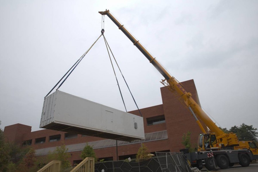 A yellow lift drops a white shipping container next to a brick building. 