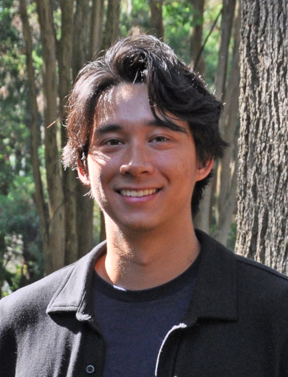 Portrait of Griffin Fish wearing a black jacket and a navy t-shirt in front of a tree