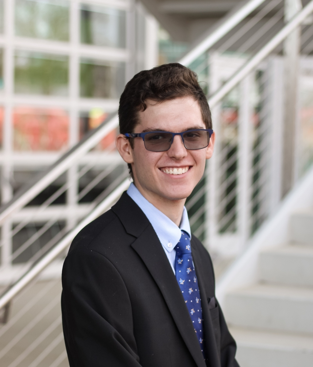 Portrait of Nate Miller in a suite with a bright blue tie and wearing sunglasses