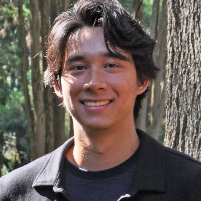 Portrait of Griffin Fish wearing a black jacket and a navy t-shirt in front of a tree