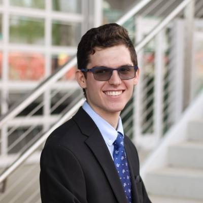 Portrait of Nate Miller in a suite with a bright blue tie and wearing sunglasses