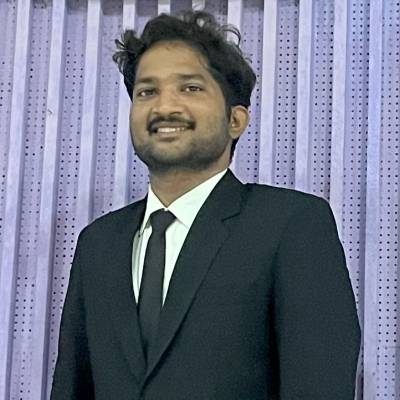 Portrait of Ramoji Rao in a blach suit and tie standing in front of a perforated steel screen