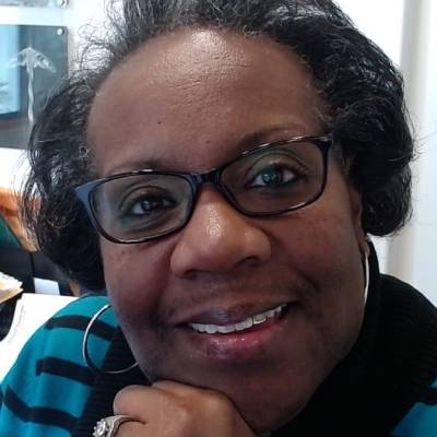 Portrait of LaShone Simmons in glasses, big hoop earrings and a blue striped sweater